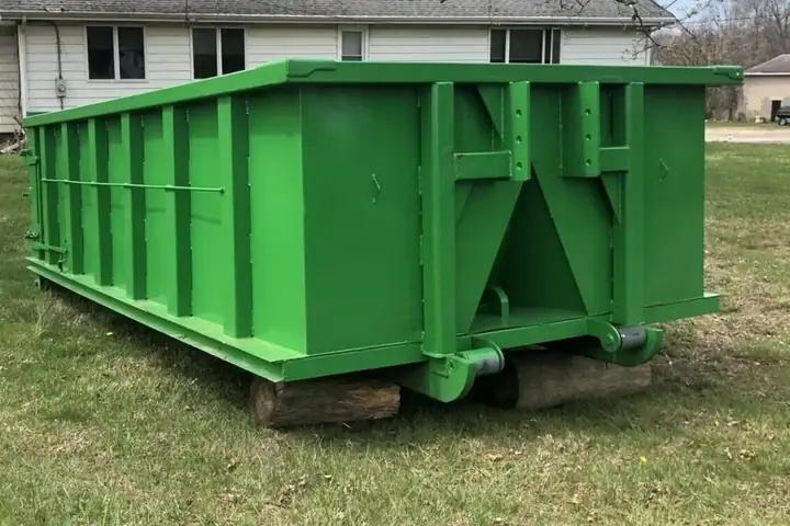 Roll-off dumpster set on wood boards on grass beside a house